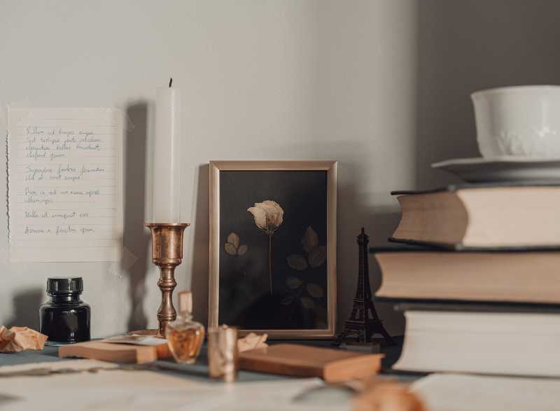 A rustic collection of old books, candles, calligraphy pens and a cup of tea perched on a desk. All farmhouse decor.