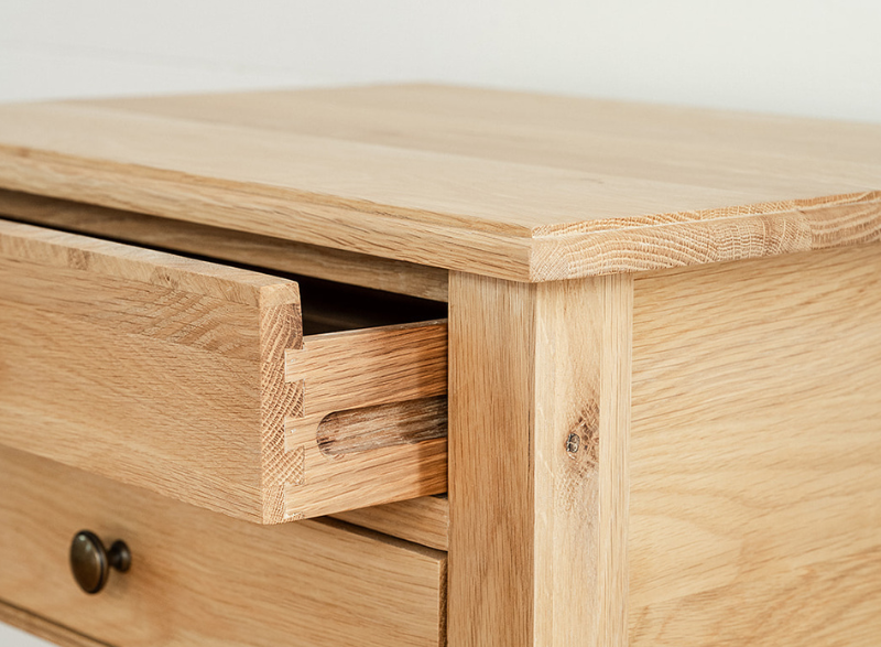 A Chloe Bedside Table in Oak, with a drawer partially open and a close up of the grain of wood. 